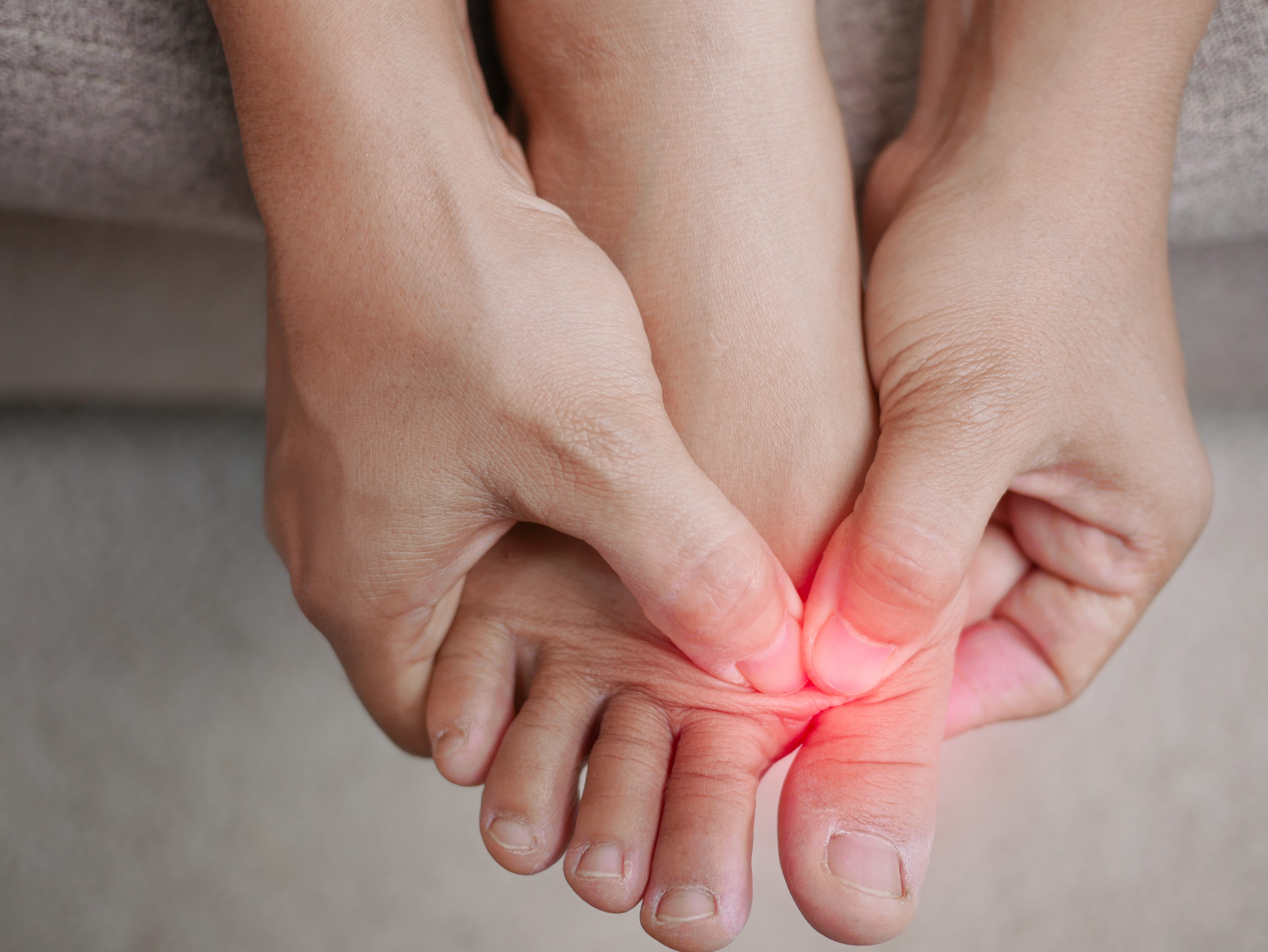 Closeup of female holding her painful feet and massaging her toes to relieve pain.