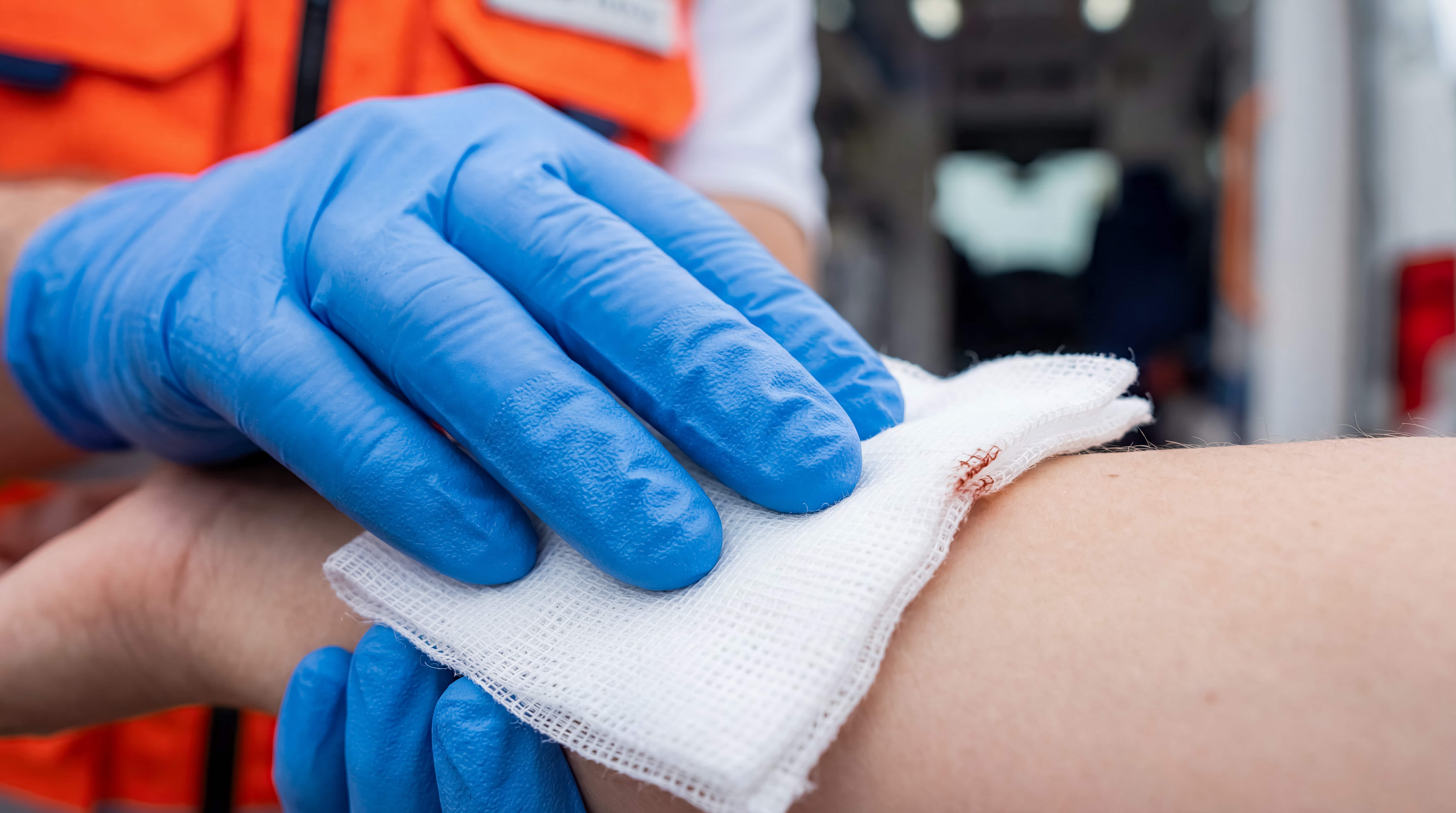 Emergency medical technician pressing clean bandage onto bloody wound on patient body near ambulance vehicle concept of rapid healthcare response first aid treatment and professional rescue